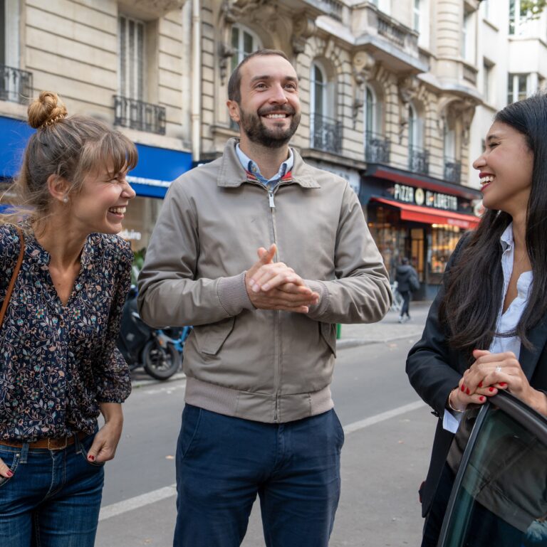 un groupe d'amis souriant dans la rue, un homme et 2 femmes