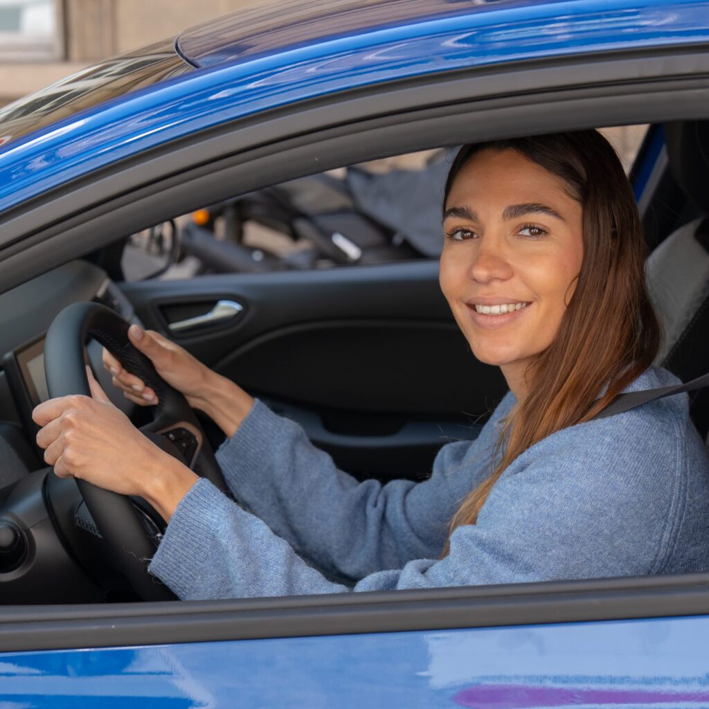 jeune femme souriant au volant de sa voiturer auto-école