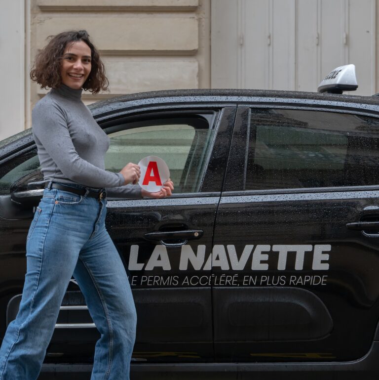 une fille brandit son disque jeune conducteur devant sa voiture d'auto-école La Navette