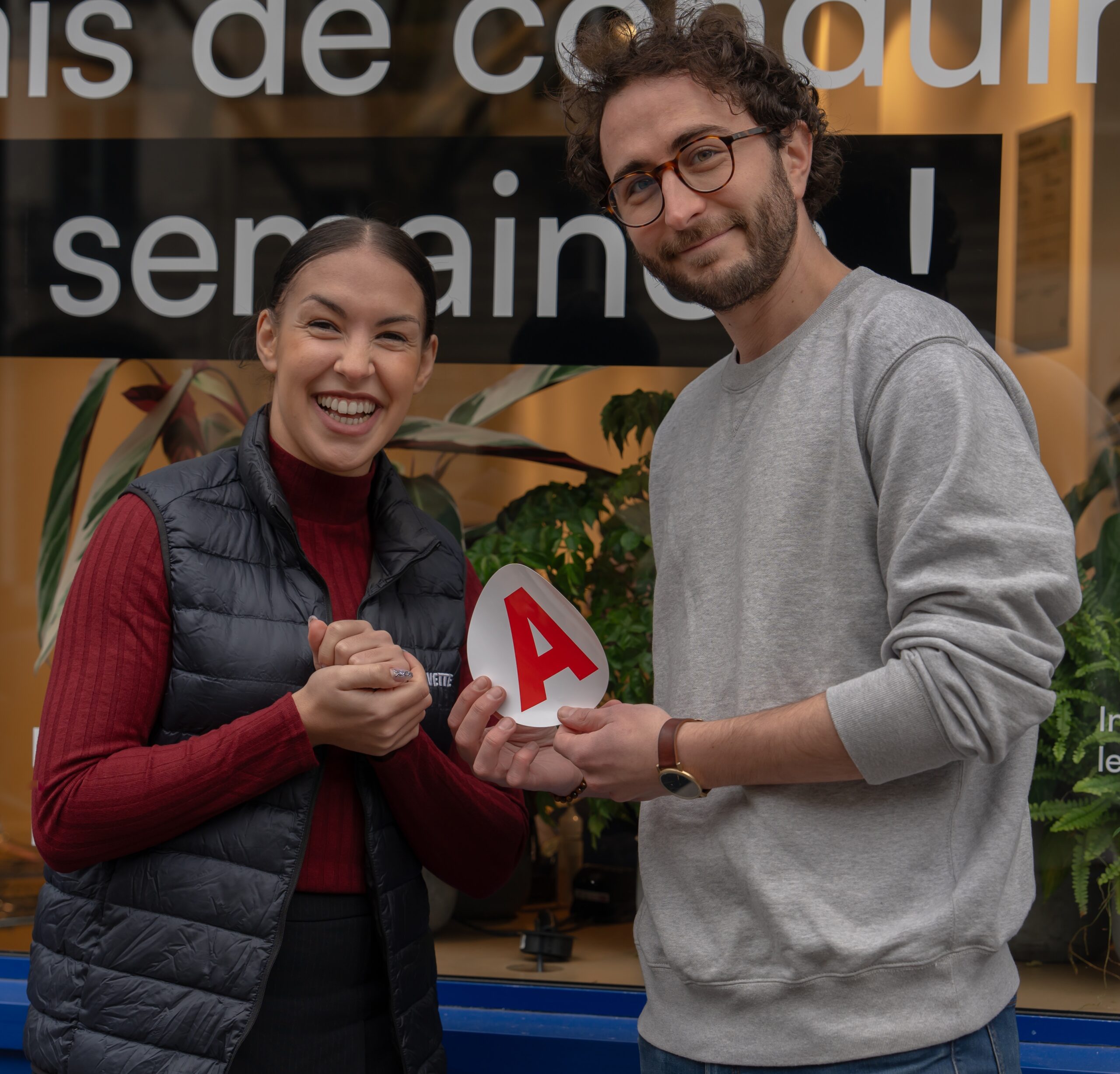 jeune homme et jeune femme souriant devant la vitrine de l'auto-école La Navette
