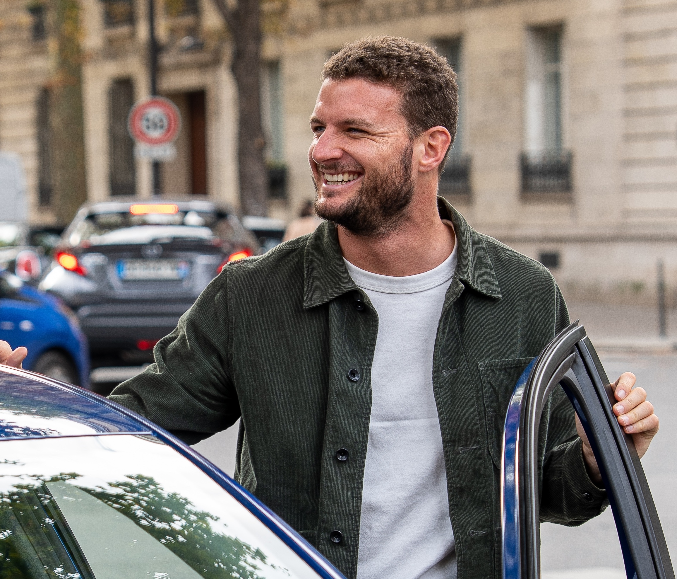 un jeune homme souriant rentre dans sa voiture